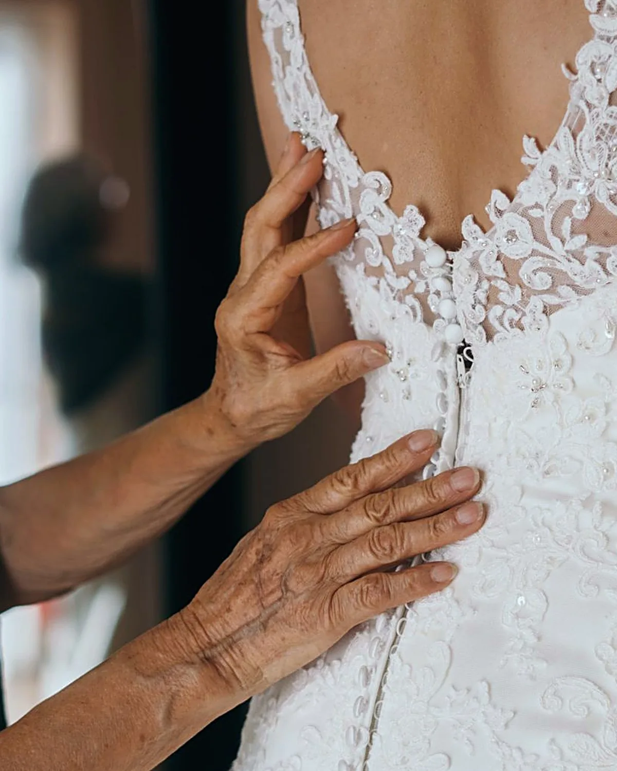 A seamstress's hands checking the fit down the fastened back of a lace bridal gown
