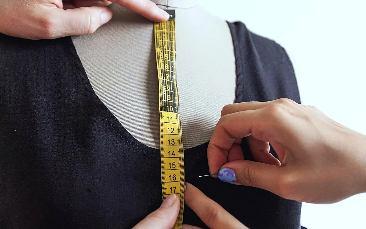 A tape measure run down the front of a black dress on a dress form