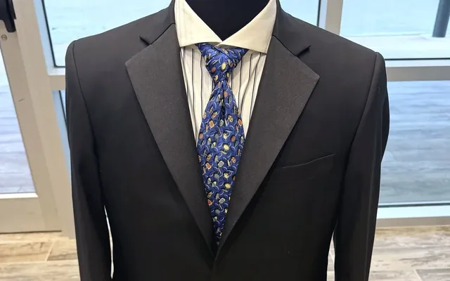 A finished black dinner jacket with striped shirt and patterned tie on the shop's form