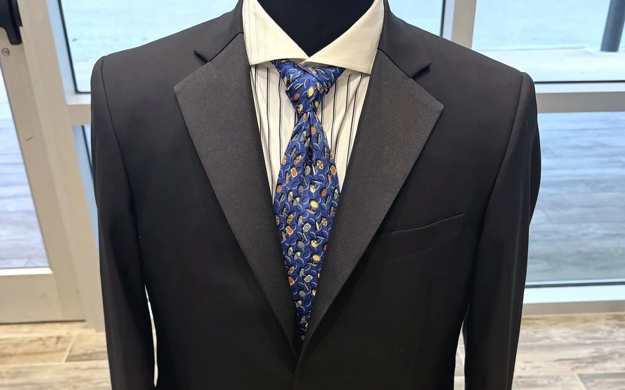 A finished black dinner jacket with striped shirt and patterned tie on the shop's form
