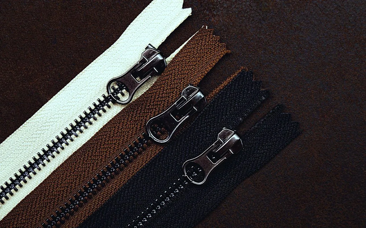 Three replacement zippers in cream, brown and black laid on dark leather