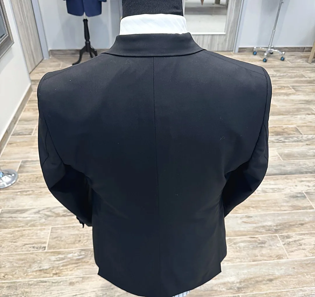 A finished black jacket seen from the back on the shop's dress form