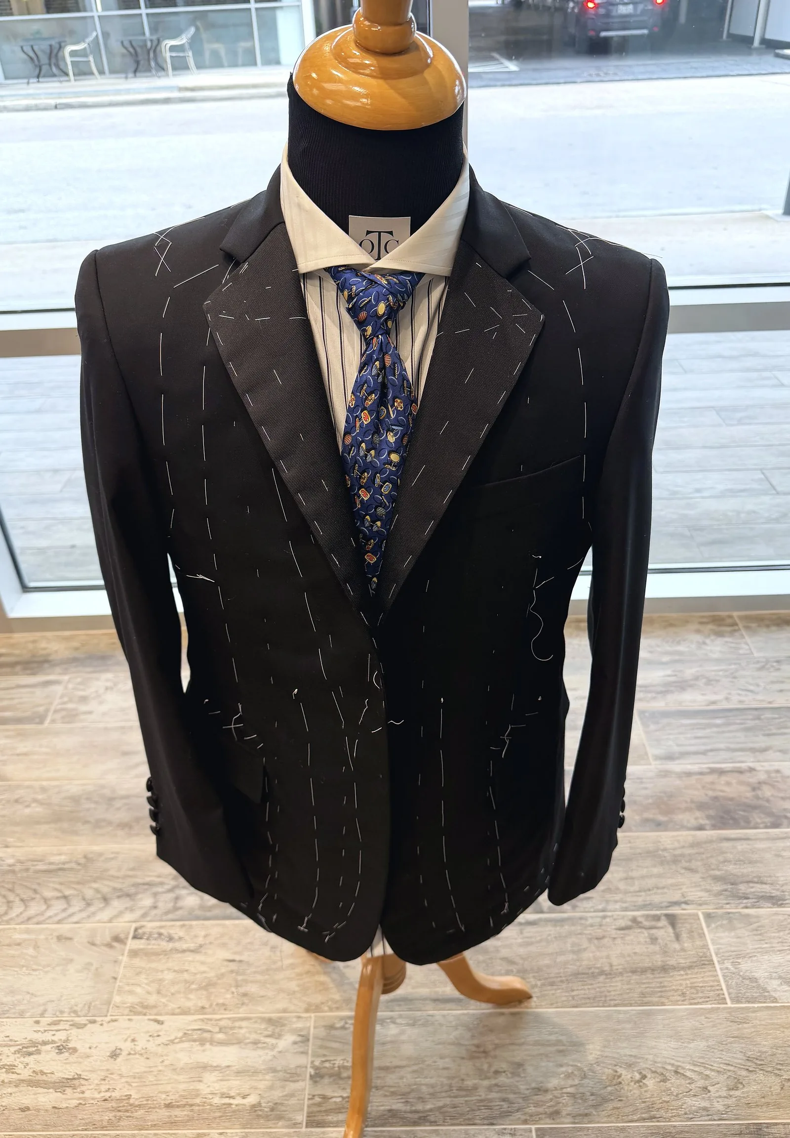 A black dinner jacket covered in white basting and marking lines, on the shop's form
